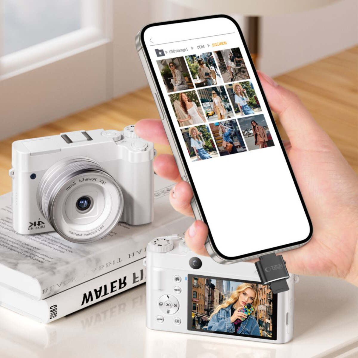 Un appareil photo blanc sur un livre. Un téléphone affiche des photos, tenu par une main. Un autre appareil photo montre une photo. Un adaptateur USB est connecté.