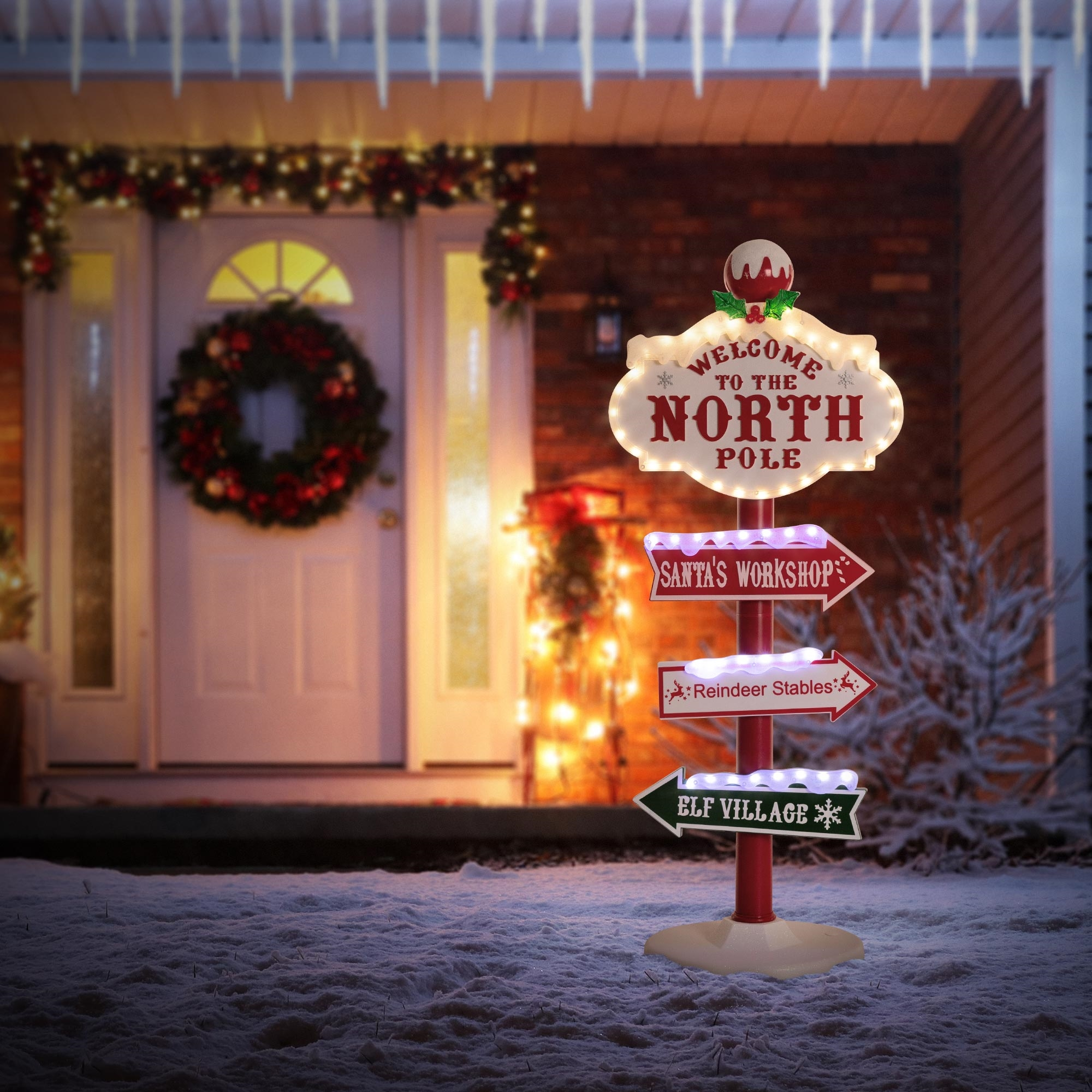 Ein Nordpol-Schild weist auf Santa's Werkstatt, Rentierstallungen und das Elfen-Dorf hin. Ein Kranz und Lichter schmücken das Haus.