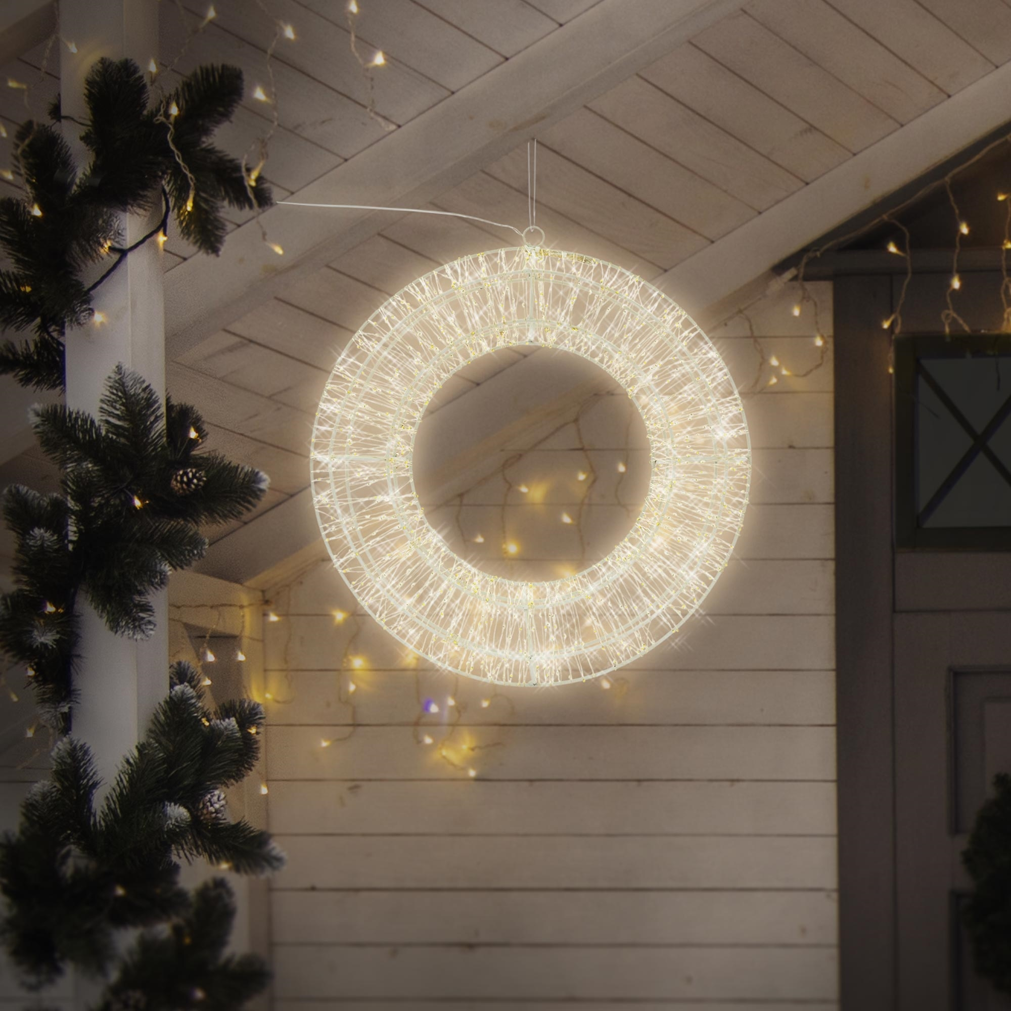 Ein leuchtender, kreisförmiger Weihnachtskranz hängt an einer Veranda. Tannenzweige und Lichter rahmen die Szene ein und schaffen ein festliches Ambiente.