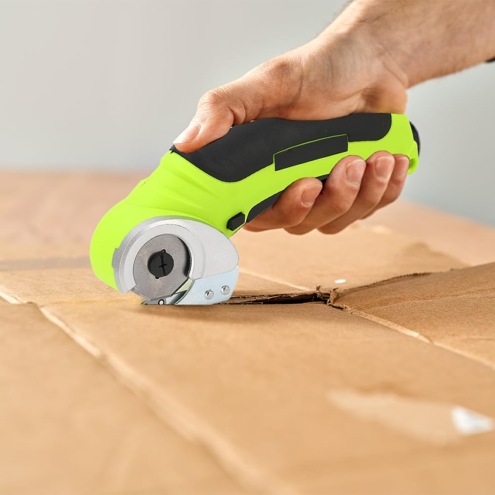 Eine Hand hält einen grün-schwarzen elektrischen Schneider, der Pappe schneidet. Der Schneider hat eine kreisförmige Klinge. Der Hintergrund ist unscharf.