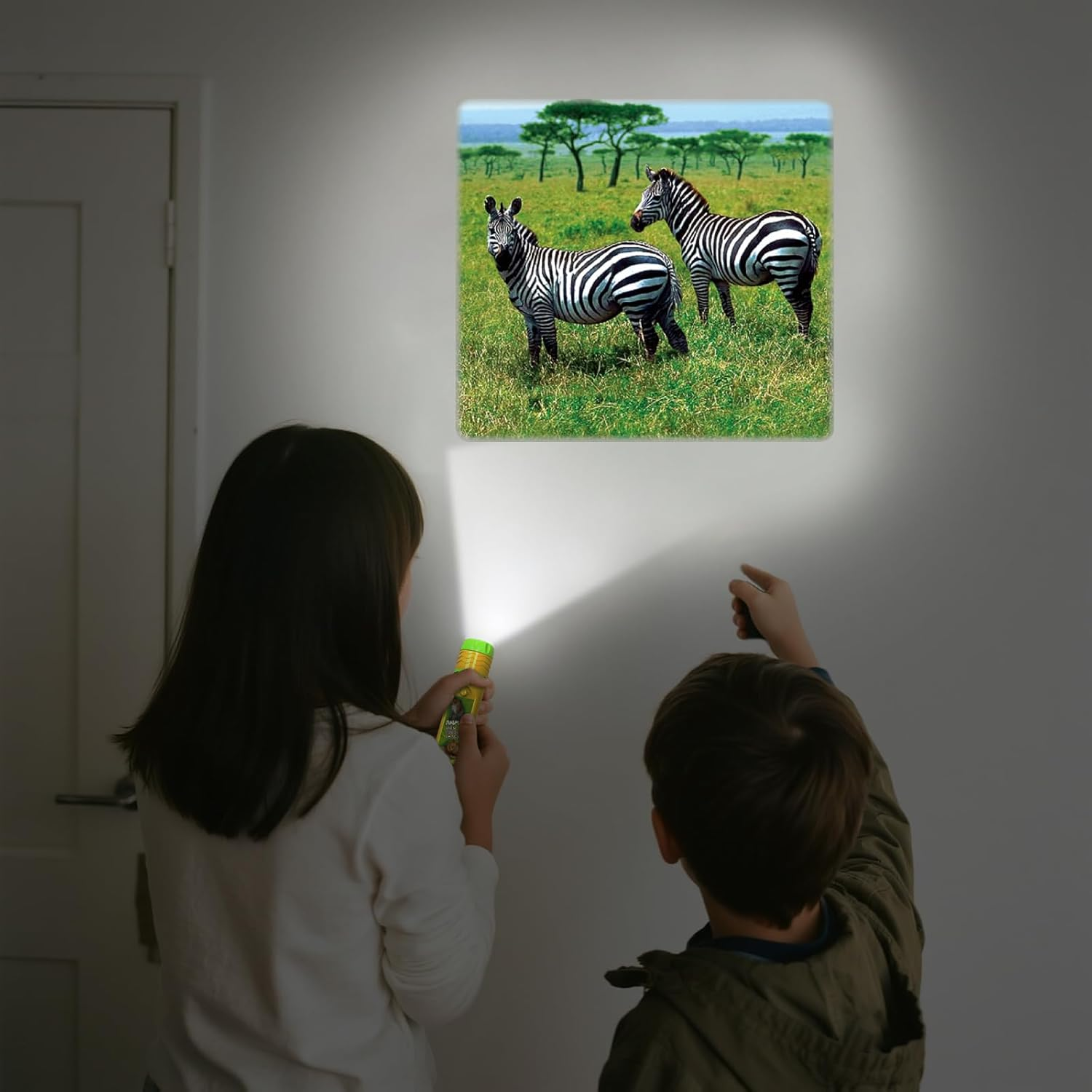 Zwei Kinder leuchten mit Taschenlampen auf ein Zebra-Bild an der Wand. Das Bild zeigt zwei Zebras auf einer Wiese.