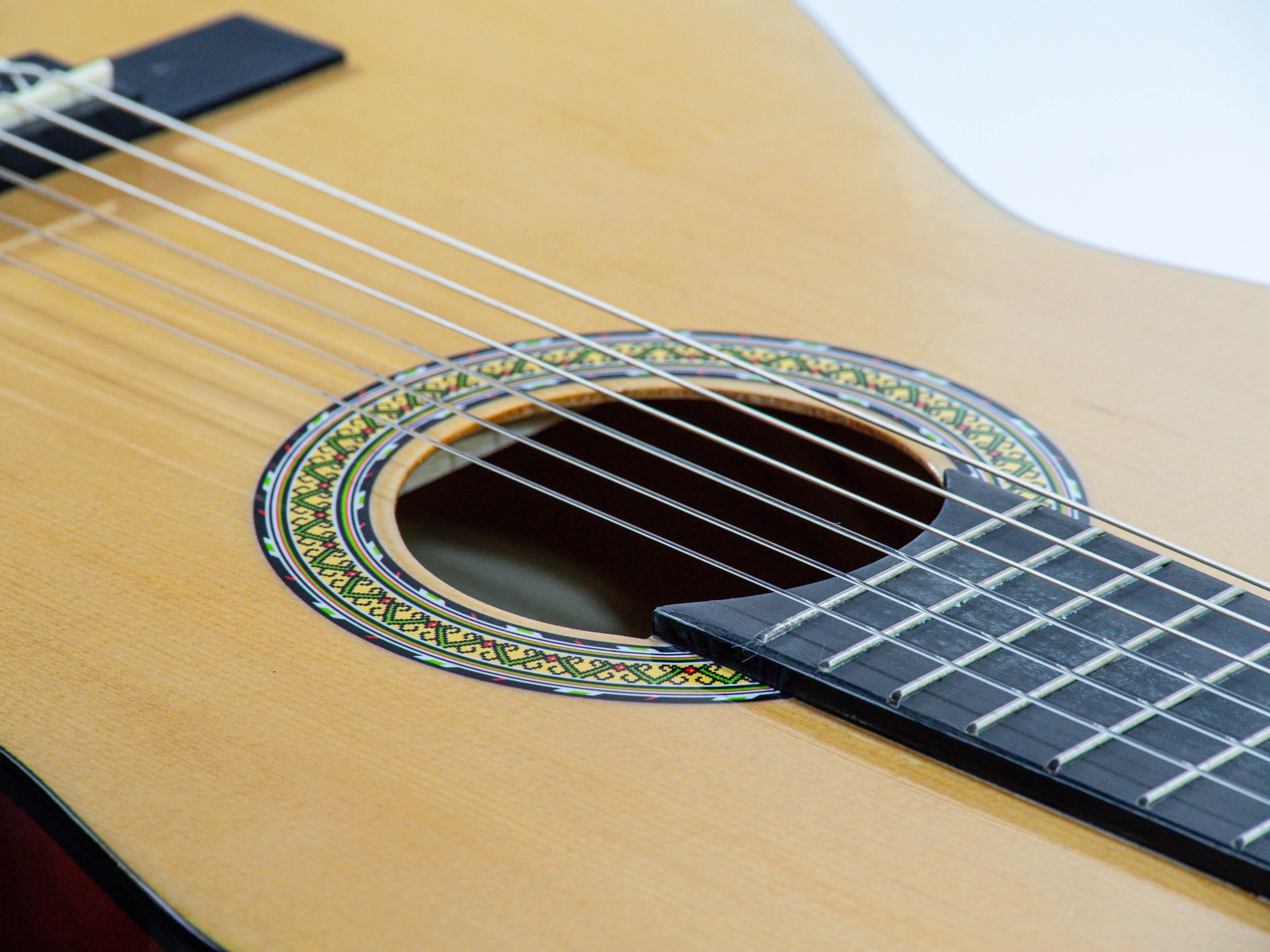 Nahaufnahme einer klassischen Gitarre. Sichtbar sind Saiten, Griffbrett, Schallloch und Holzkorpus mit Zierleisten.