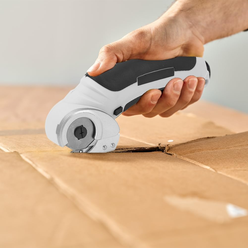 Eine Hand hält einen weiß-schwarzen Rollenschneider, der durch einen Karton schneidet. Der Hintergrund ist eine schlichte Wand.