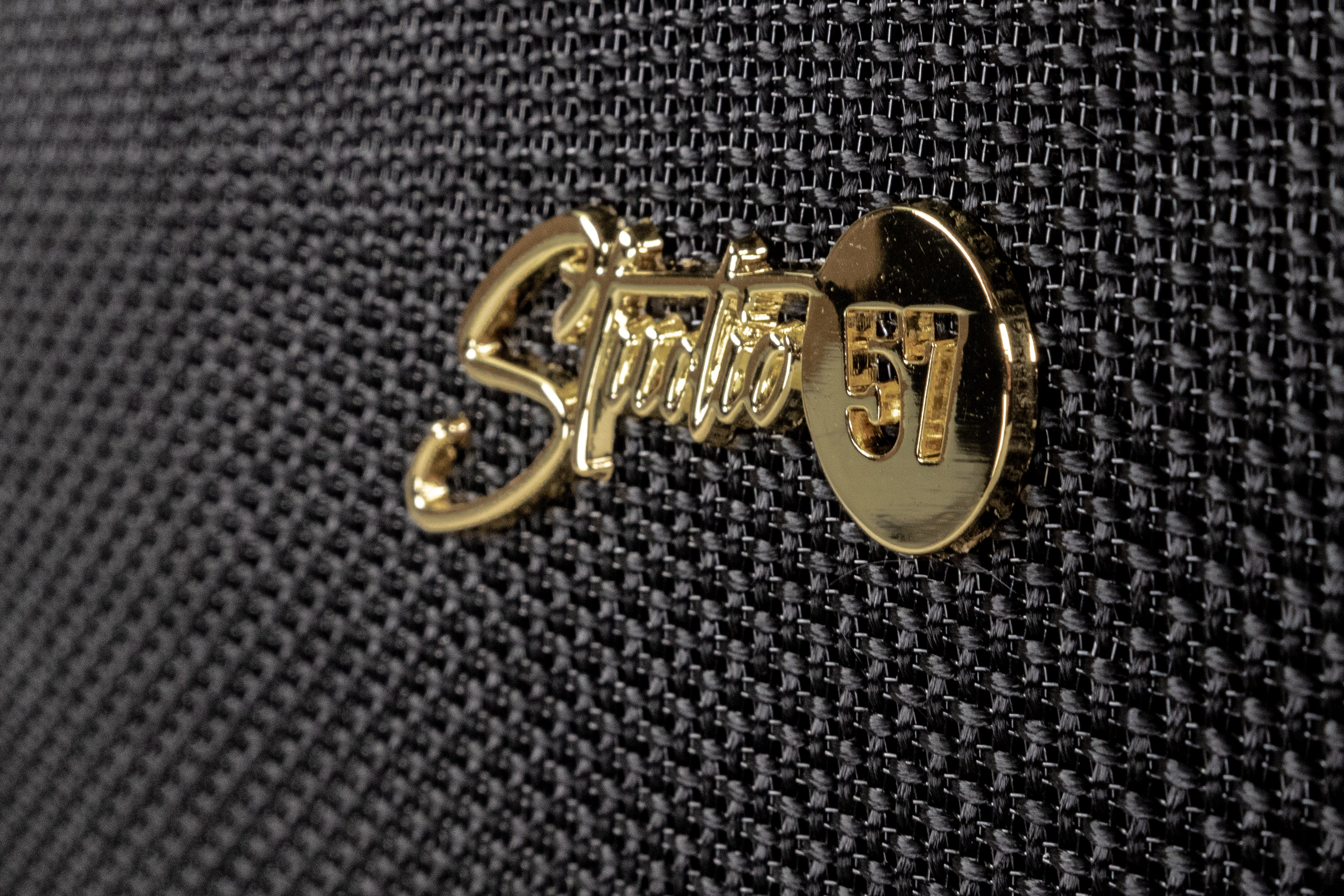 Nahaufnahme eines Lautsprechergrills mit einem goldenen 'Studio 57' Abzeichen. Der Grill ist aus schwarzem, strukturiertem Stoff.