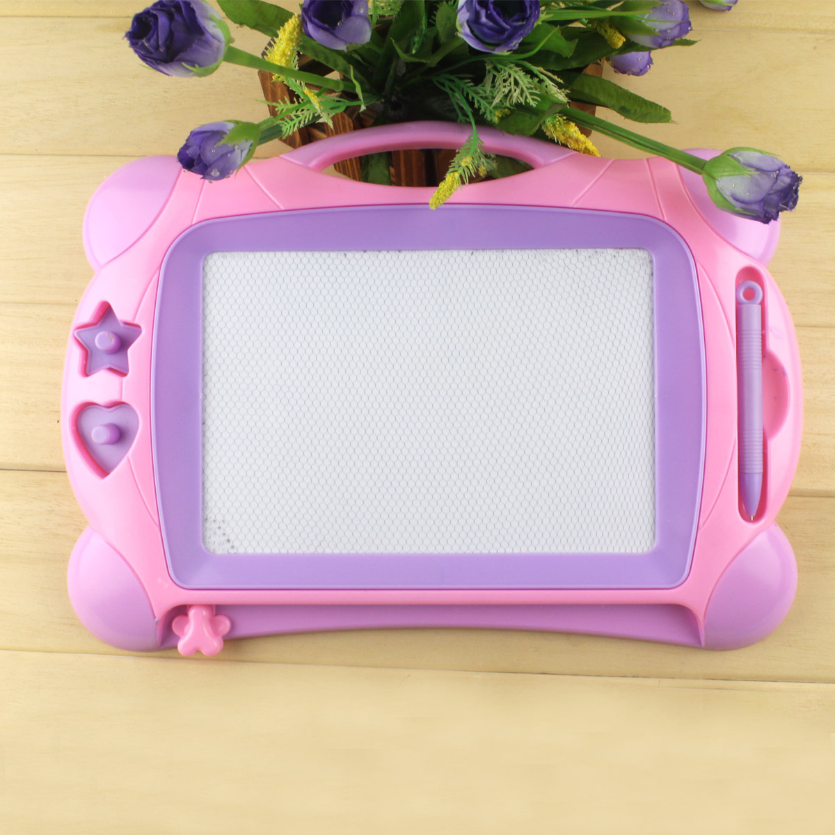 Eine rosa-violette Zeichenfläche mit weißem Bildschirm, Stift und Blumen auf Holz.