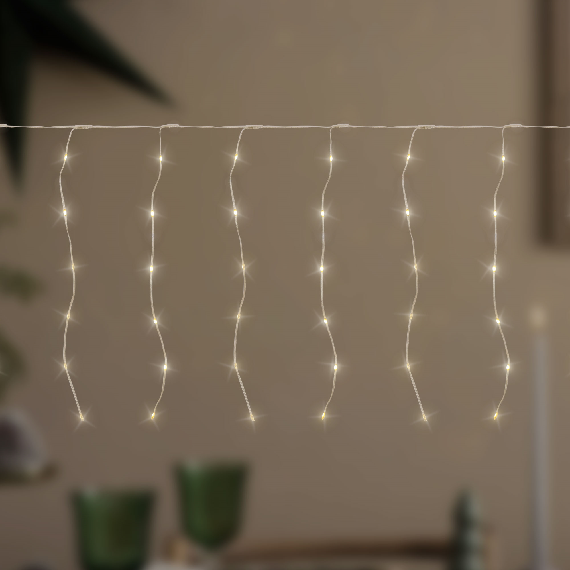 Eine Lichterkette mit warmweißen Lichtern, die vor einem verschwommenen Hintergrund hängt. Die Lichter sind gleichmäßig verteilt.