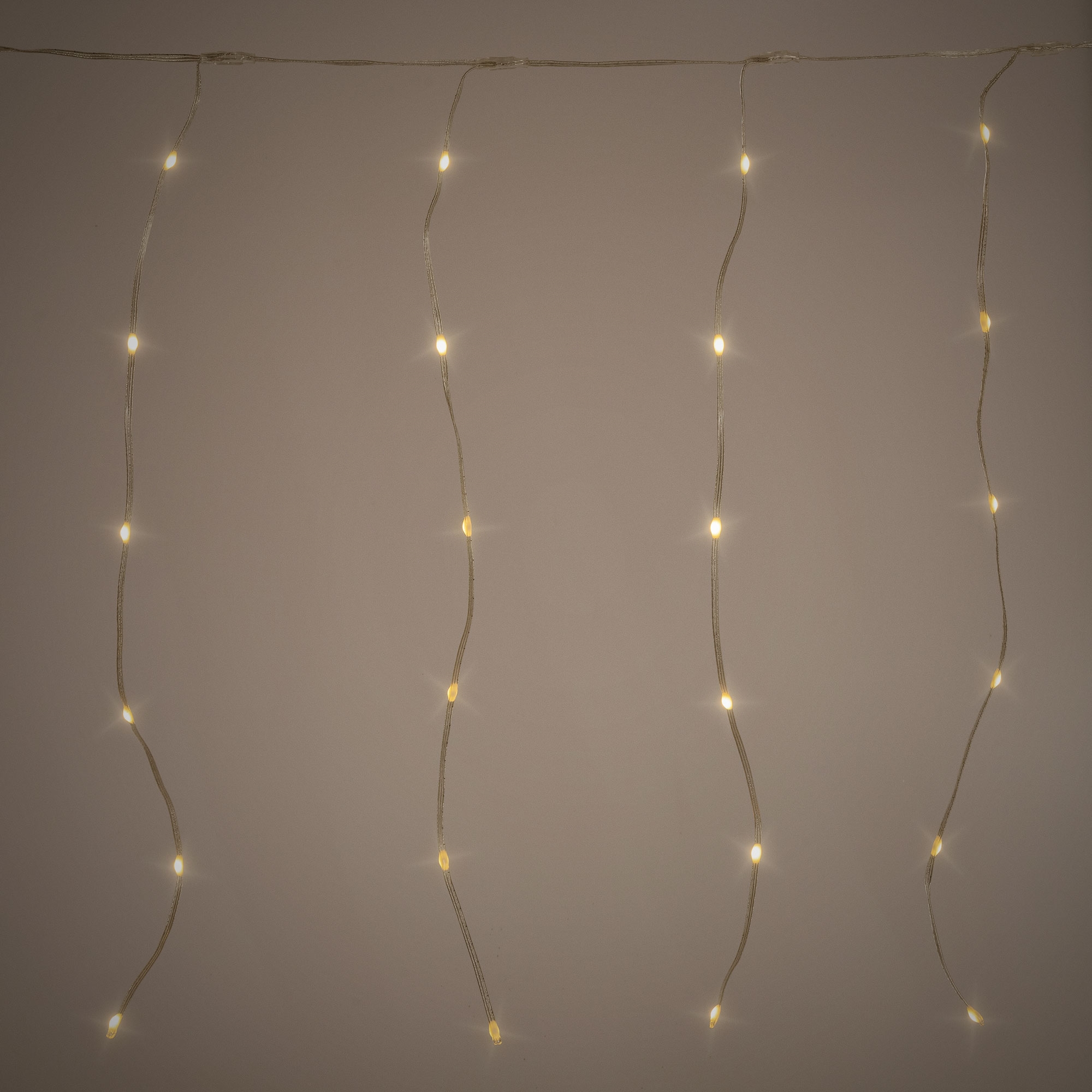 Lichterkette mit kleinen, warmweißen LEDs vor einem beigefarbenen Hintergrund. Die Lichter sind gleichmäßig verteilt.
