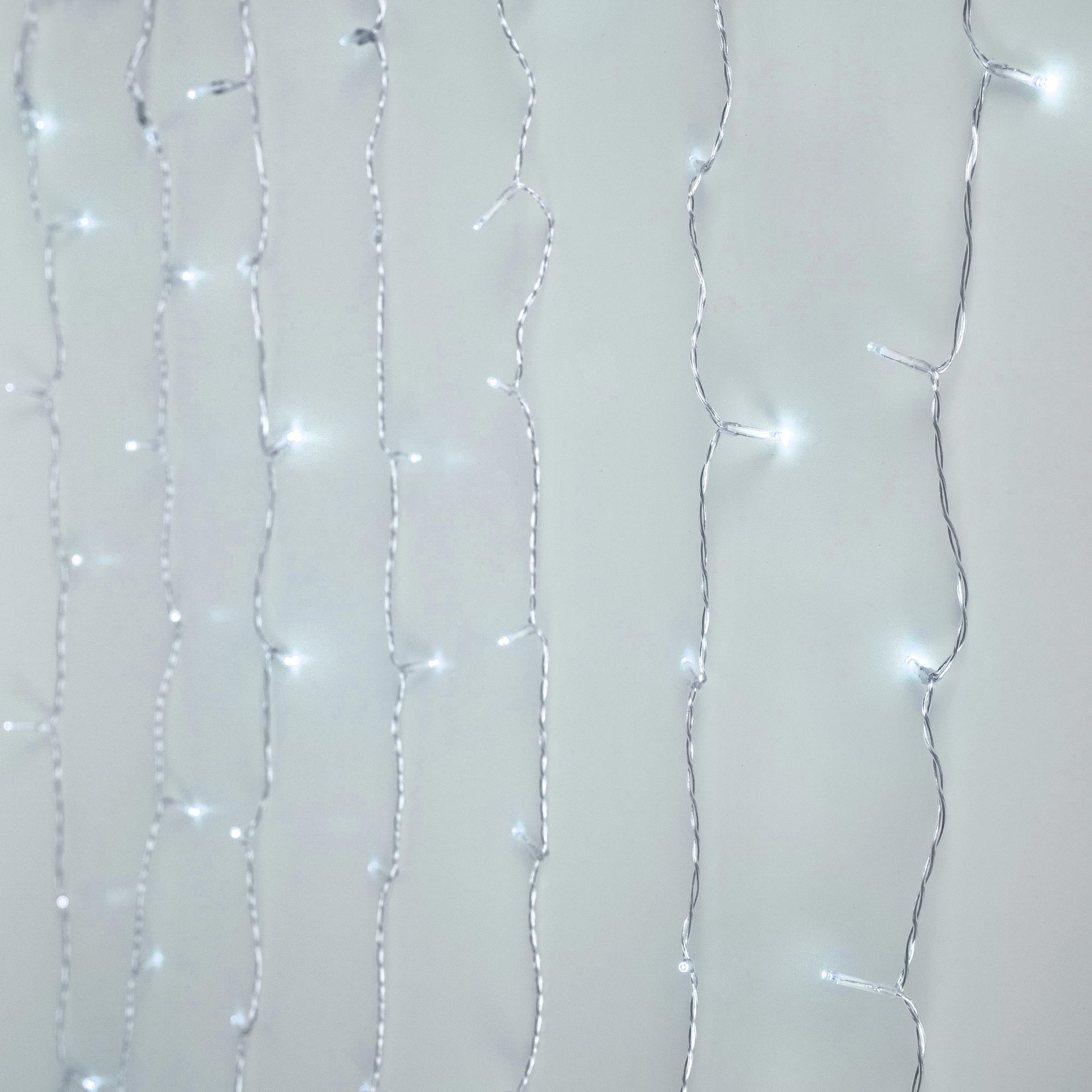 Nahaufnahme von Lichterketten vor weißem Hintergrund. Kleine, helle, weiße LEDs sind auf dünnen Silberdrähten angeordnet.