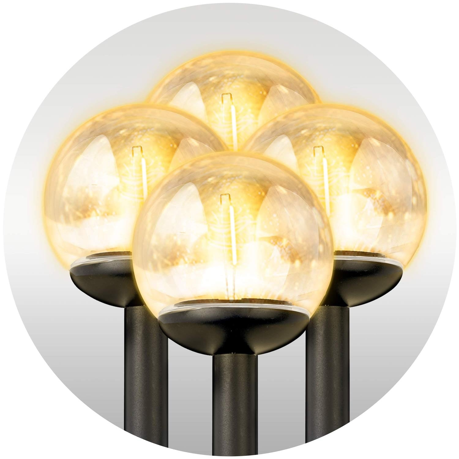 Cuatro luces esféricas iluminadas con un brillo amarillo cálido, montadas en postes negros, dispuestas en círculo.