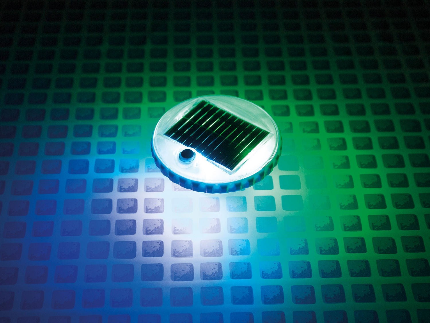 Un panel solar redondo con un panel negro está sobre una superficie con patrones cuadrados. El fondo gradúa de azul a verde.