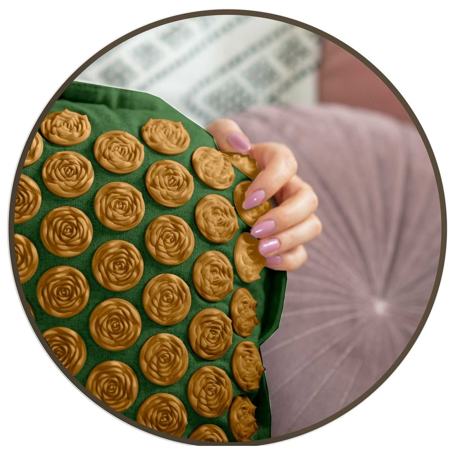Una mano sostiene un cojín verde cubierto de nodos de masaje dorados en forma de rosa. El fondo incluye una almohada y una superficie estampada.