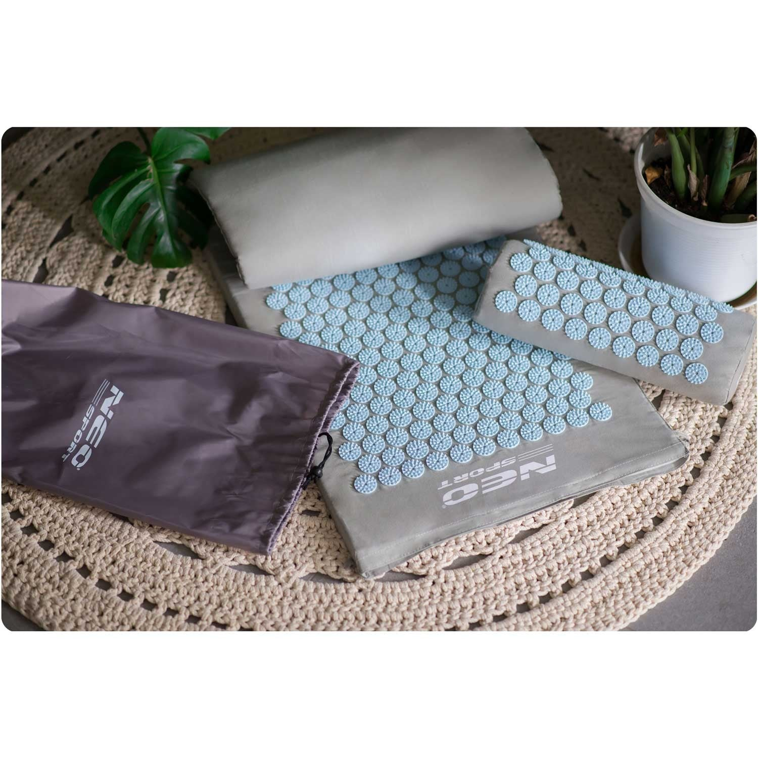 Esterillas de acupresión y una almohada con púas azules, una bolsa gris y una planta sobre una alfombra beige.