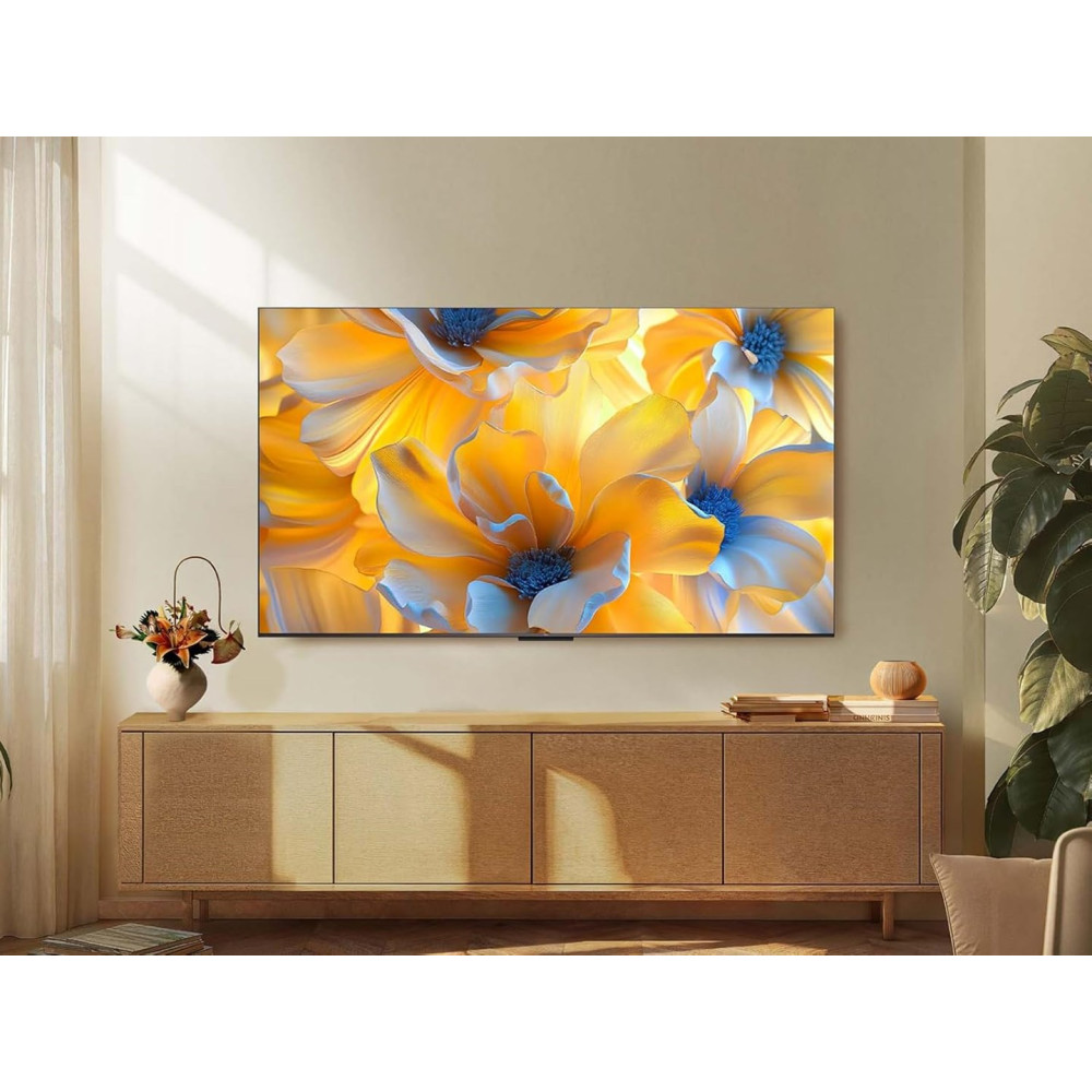 Telewizor wyświetla żółtą i niebieską grafikę kwiatową. Znajduje się nad drewnianą szafką z dekoracjami i roślinami.