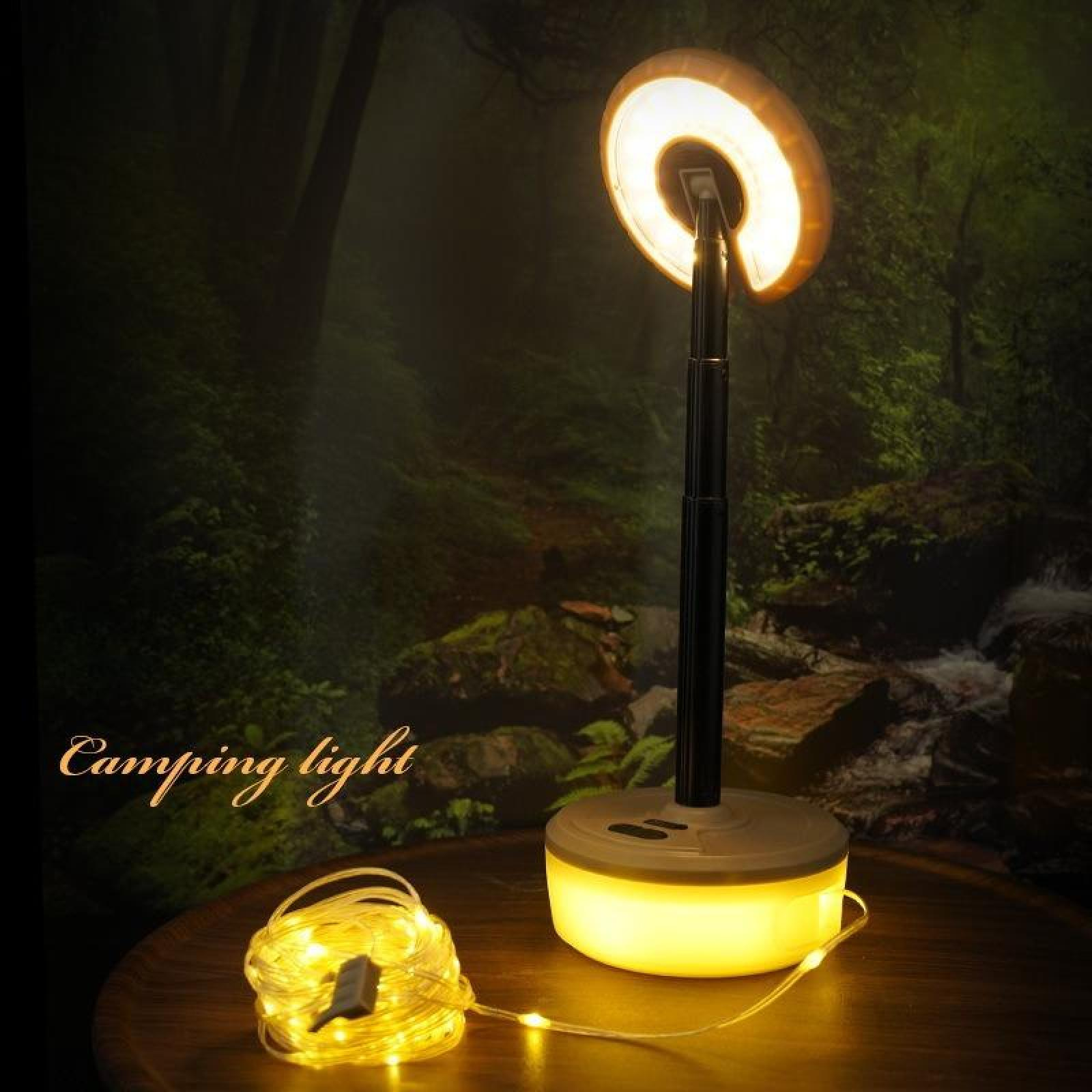 Eine Campinglampe mit kreisförmigem Leuchtkopf, auf einem Holztisch, mit Lichterketten und einem Waldhintergrund.