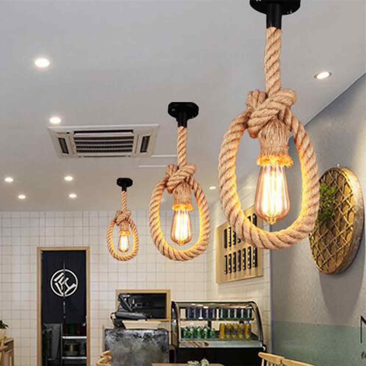 Drei Pendelleuchten im Seil-Stil mit Edison-Glühbirnen hängen von der Decke. Ein Café mit einem dekorativen Wandstück und einer Theke.