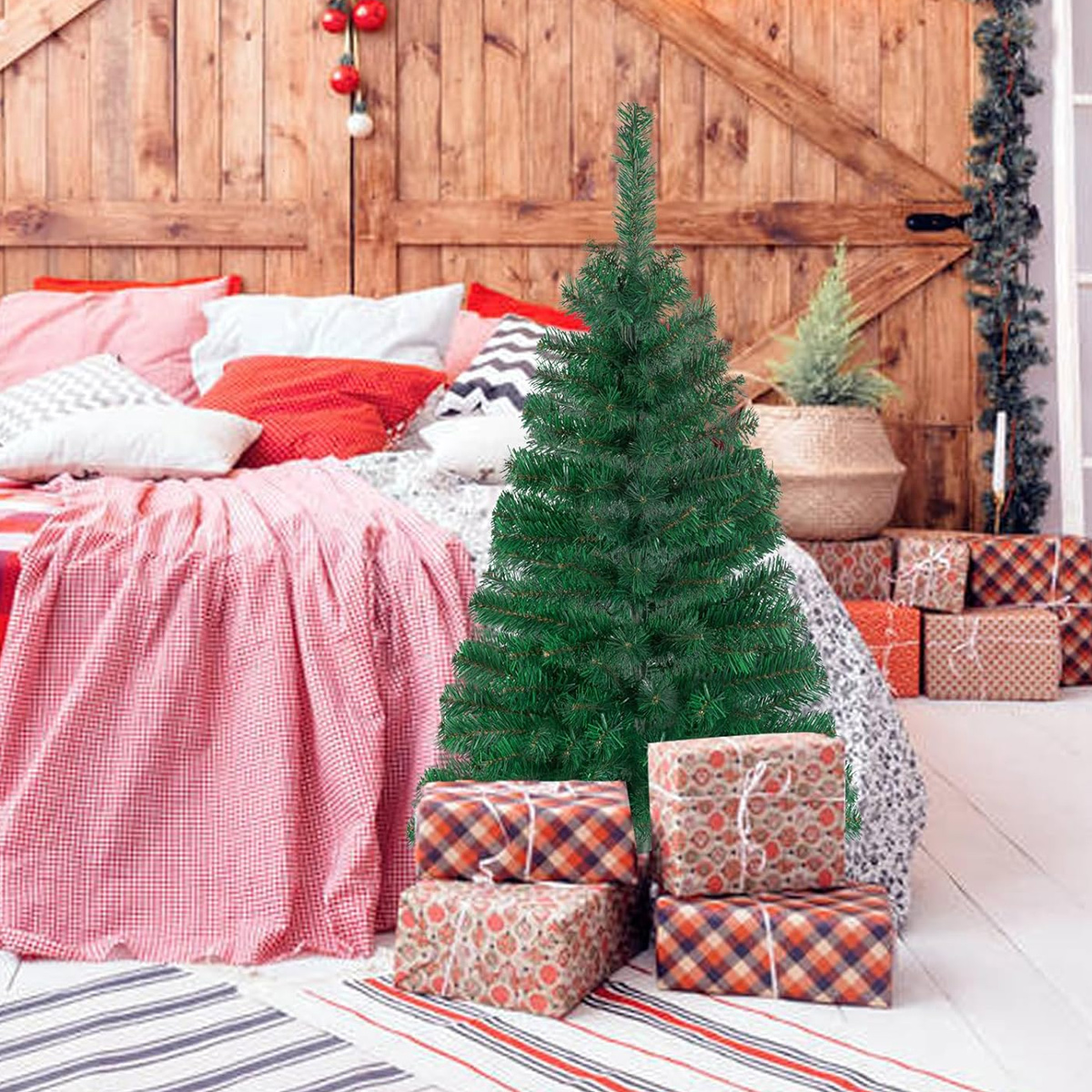 Ein grüner Weihnachtsbaum steht vor einem Bett mit roter Bettwäsche und Kissen. Geschenkverpackungen stehen vor dem Baum. Der Hintergrund ist eine Holzwand.