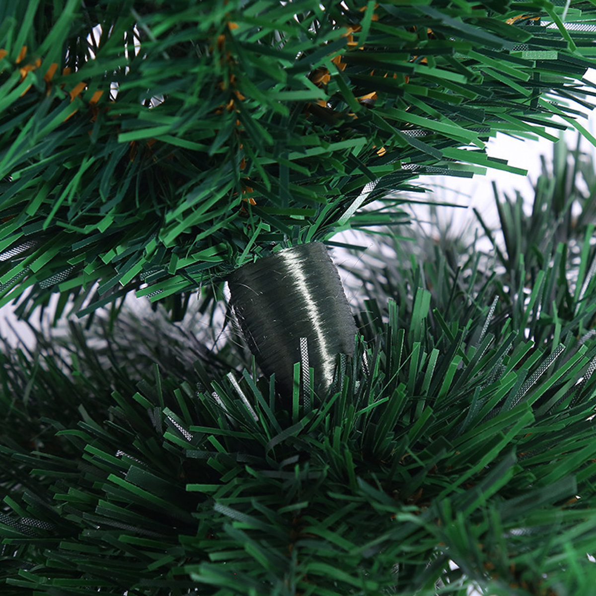 Nahaufnahme eines grünen künstlichen Weihnachtsbaumzweigs. Ein silberner Draht umwickelt den Zweig. Weißer Hintergrund.