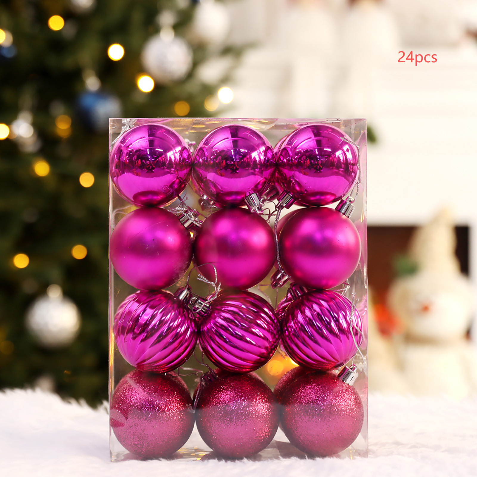 Eine Schachtel mit 24 rosa Weihnachtskugeln. Einige sind glänzend, einige matt, und einige haben Muster. Der Hintergrund ist ein Weihnachtsbaum.