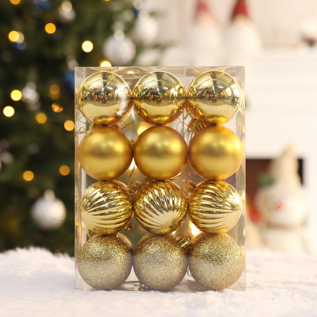 Eine transparente Box mit goldenen Weihnachtskugeln. Einige sind glatt, andere gerippt und wieder andere glitzernd. Im Hintergrund ist ein Weihnachtsbaum zu sehen.