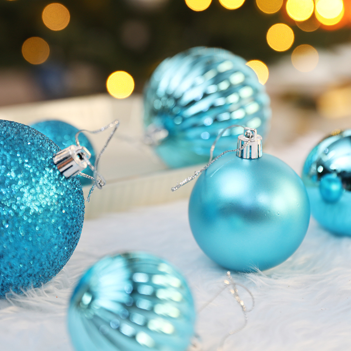 Nahaufnahme von blauen Weihnachtskugeln auf weißem Fell. Der Hintergrund hat verschwommene Lichter. Einige Ornamente sind glitzernd, andere glatt.
