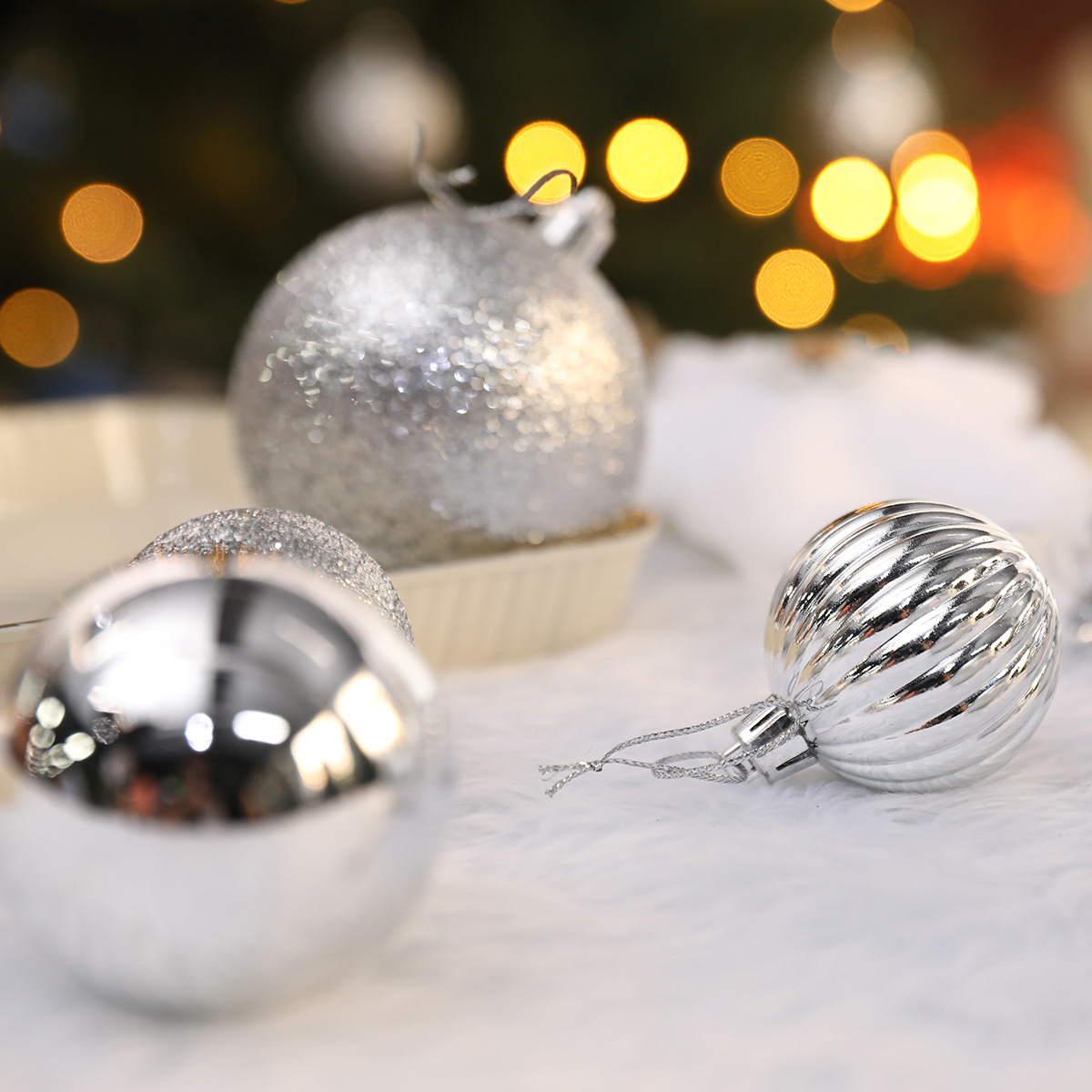 Nahaufnahme von silbernen Weihnachtsschmuck auf einer weißen, flauschigen Oberfläche. Verschwommene Bokeh-Lichter im Hintergrund. Variierende Designs.