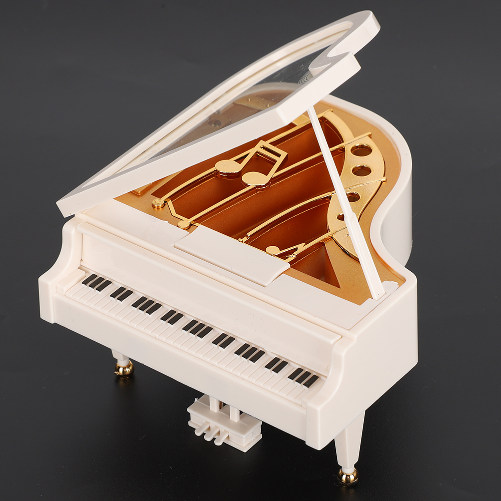 Ein weißes Spielzeug-Flügel mit goldenen Akzenten, offenem Deckel und einer Tastatur mit schwarzen und weißen Tasten, vor dunklem Hintergrund.
