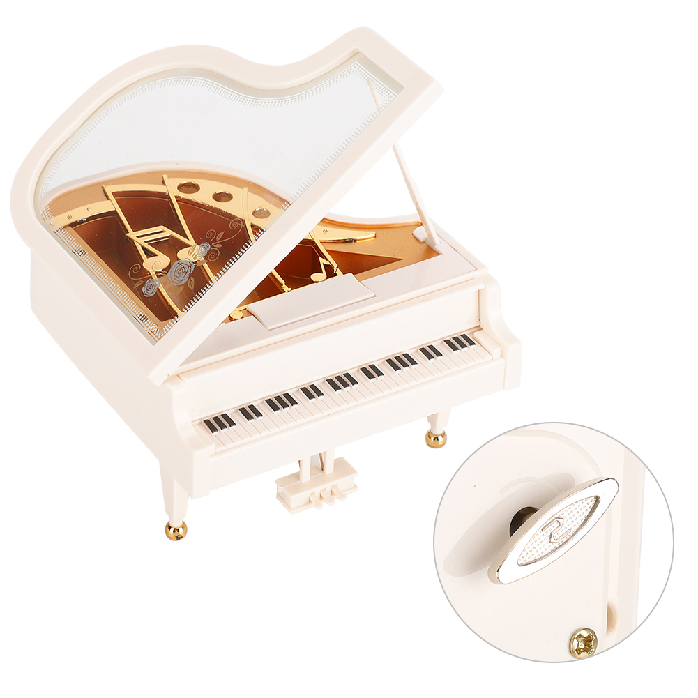 Ein weißes Spielzeug-Klavier mit offenem Deckel. Es hat eine Tastatur, goldene Akzente und einen Aufziehschlüssel. Eine kleine, detaillierte Einlage zeigt den Schlüssel.