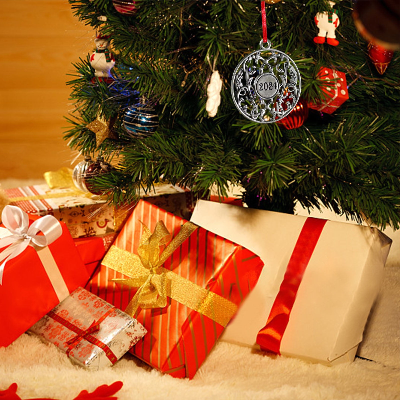 Weihnachtsbaum mit Schmuck und Geschenken. Ein 2024-Ornament hängt. Geschenke sind rot und gold, auf einem weißen Teppich.