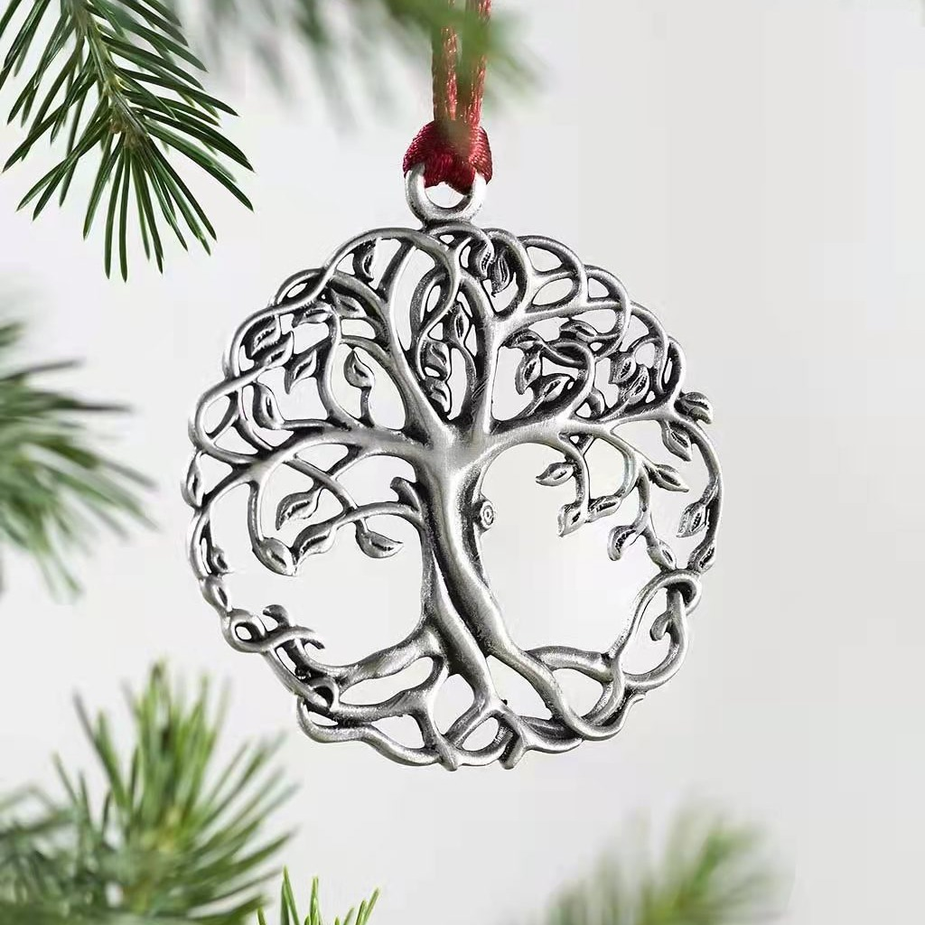 Ein silbernes Lebensbaum-Ornament hängt an einem roten Band. Grüne Tannennadeln befinden sich im Vorder- und Hintergrund vor weißem Hintergrund.