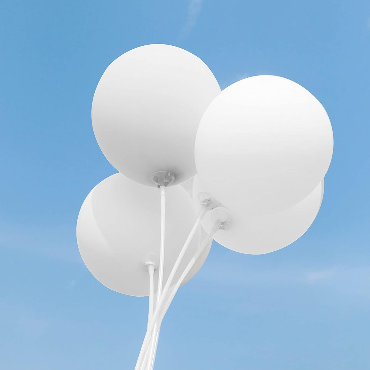 Vier weiße Ballons vor blauem Himmel. Runde Ballons, gehalten von weißen Stäben. Der Himmel ist klar.