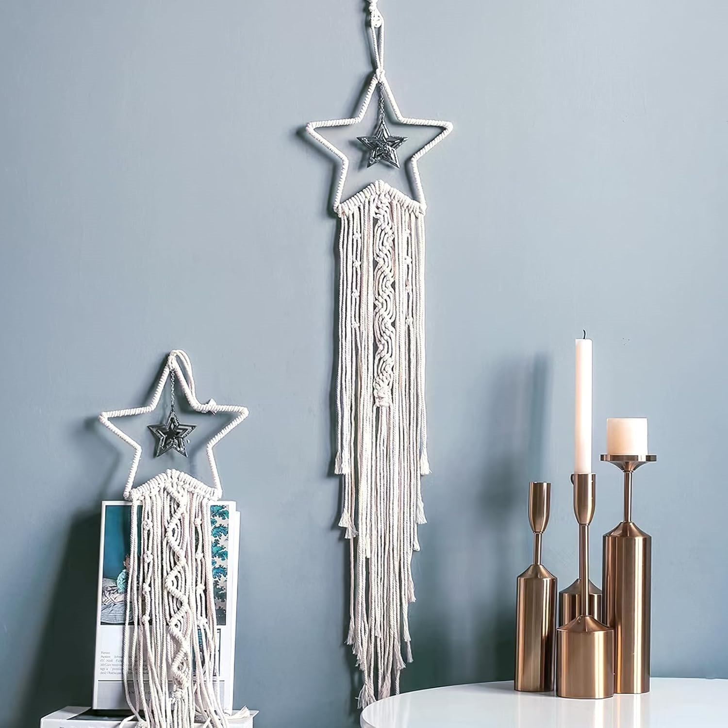 Ein sternförmiger Wandbehang mit Quasten und einem Metallstern, Kerzen und Kerzenhaltern auf einem weißen Tisch und einem Magazin.