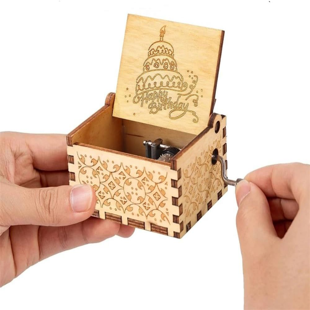 Eine hölzerne Spieluhr mit einem Geburtstagskuchen-Design. Eine Hand dreht die Kurbel. Die Box ist offen und zeigt den Mechanismus.