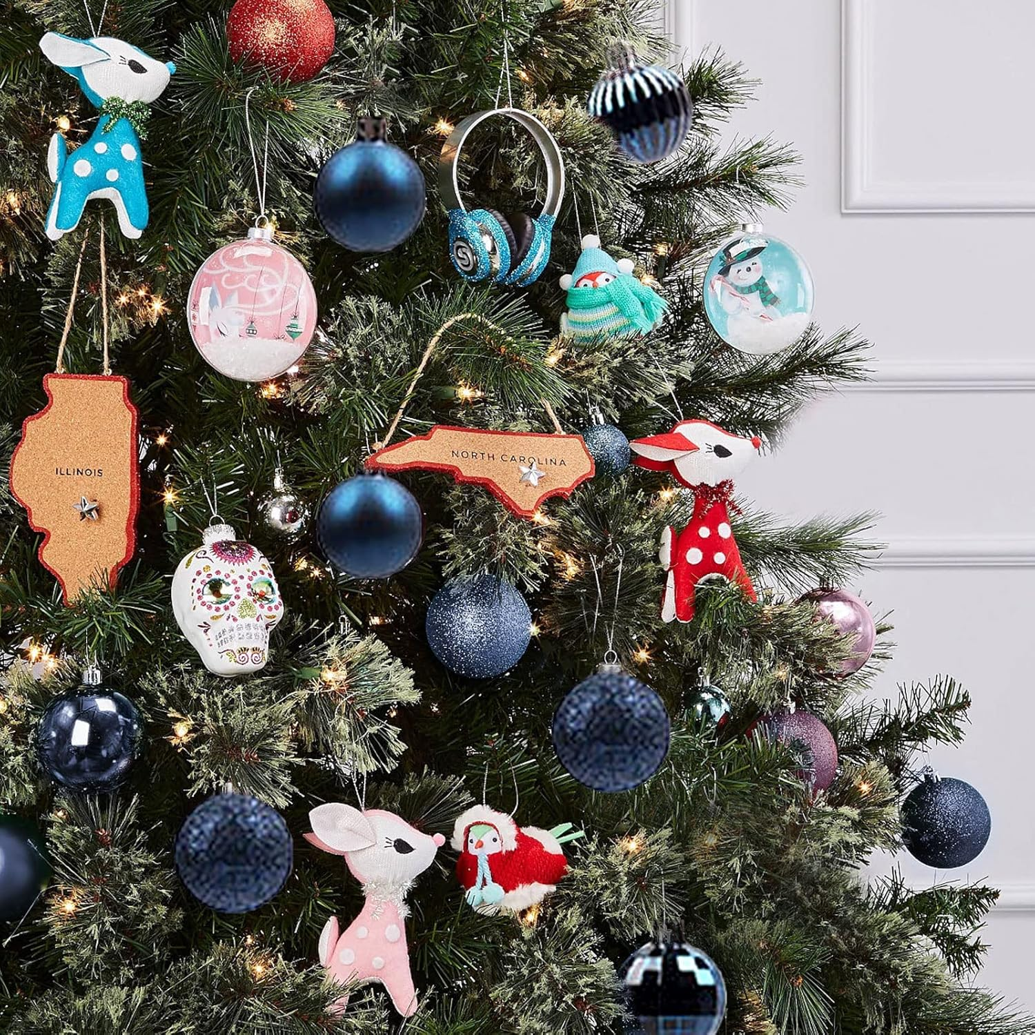 Ein geschmückter Weihnachtsbaum mit verschiedenen Ornamenten, darunter blaue, rosa und weiße Tierfiguren und Kugeln.