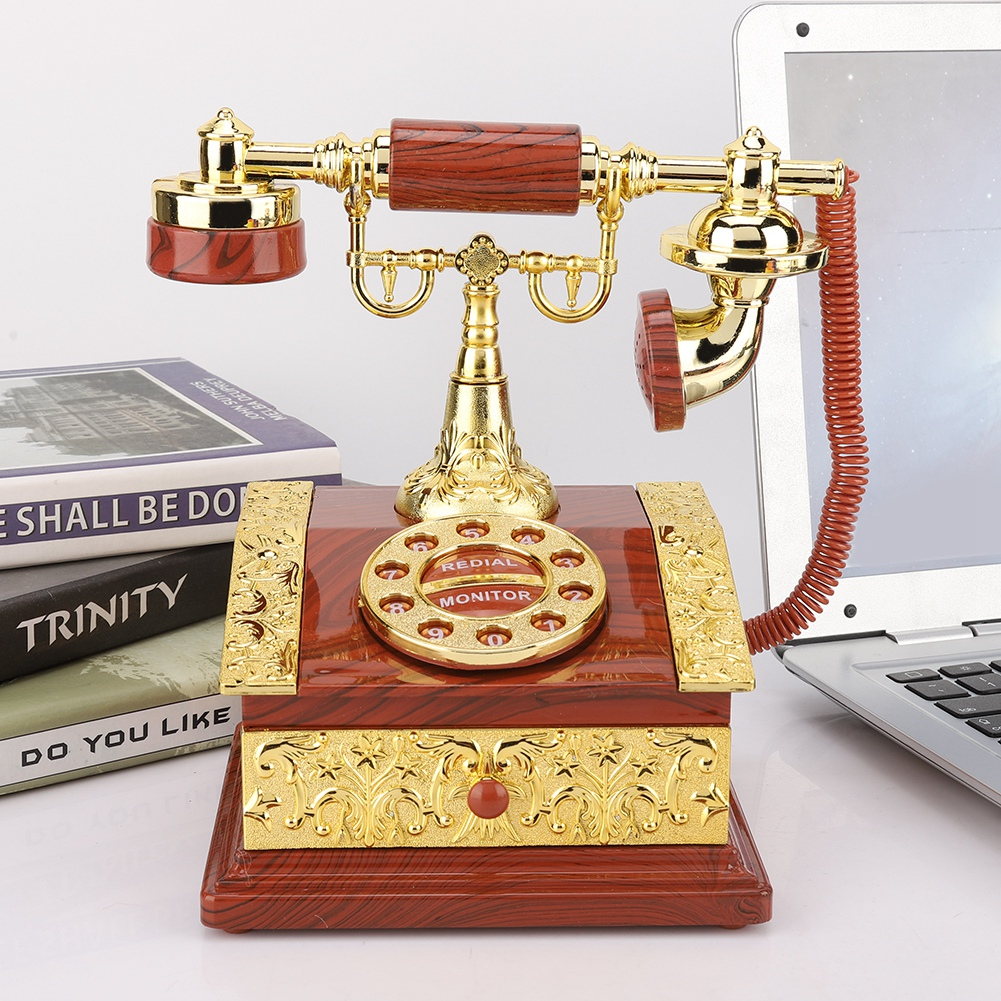 Ein antikes Telefon aus Gold und Holz steht auf einem Schreibtisch mit Büchern und einem Laptop. Das Telefon hat eine Wählscheibe.