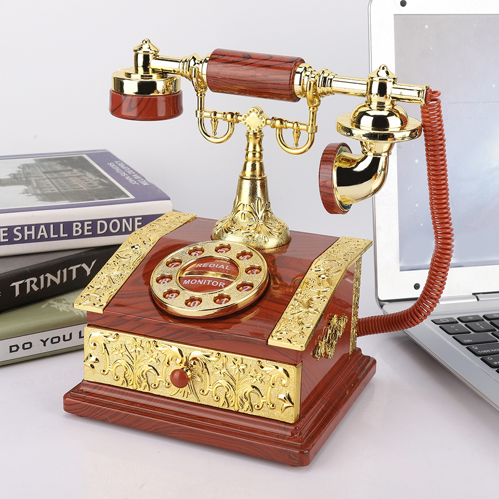 Ein antikes Telefon mit braunem Sockel und goldenen Akzenten steht neben einem Laptop und Büchern. Das Telefon hat eine Wählscheibe und ein rotes Kabel.