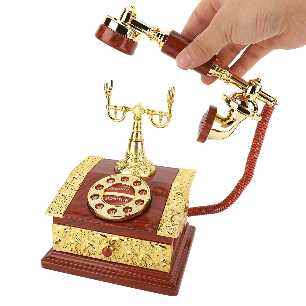 Eine Hand hält einen Vintage-Telefonhörer aus Gold und Holz. Die Basis hat ein Ziffernblatt, ein rotes Kabel verbindet den Hörer.