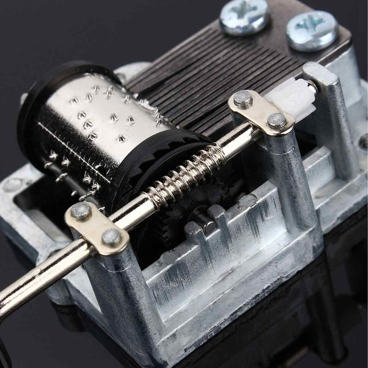 Nahaufnahme eines silbernen Spieldosenmechanismus. Eine zylindrische Trommel, Metallzinken, Zahnräder und Schrauben sind zu sehen.