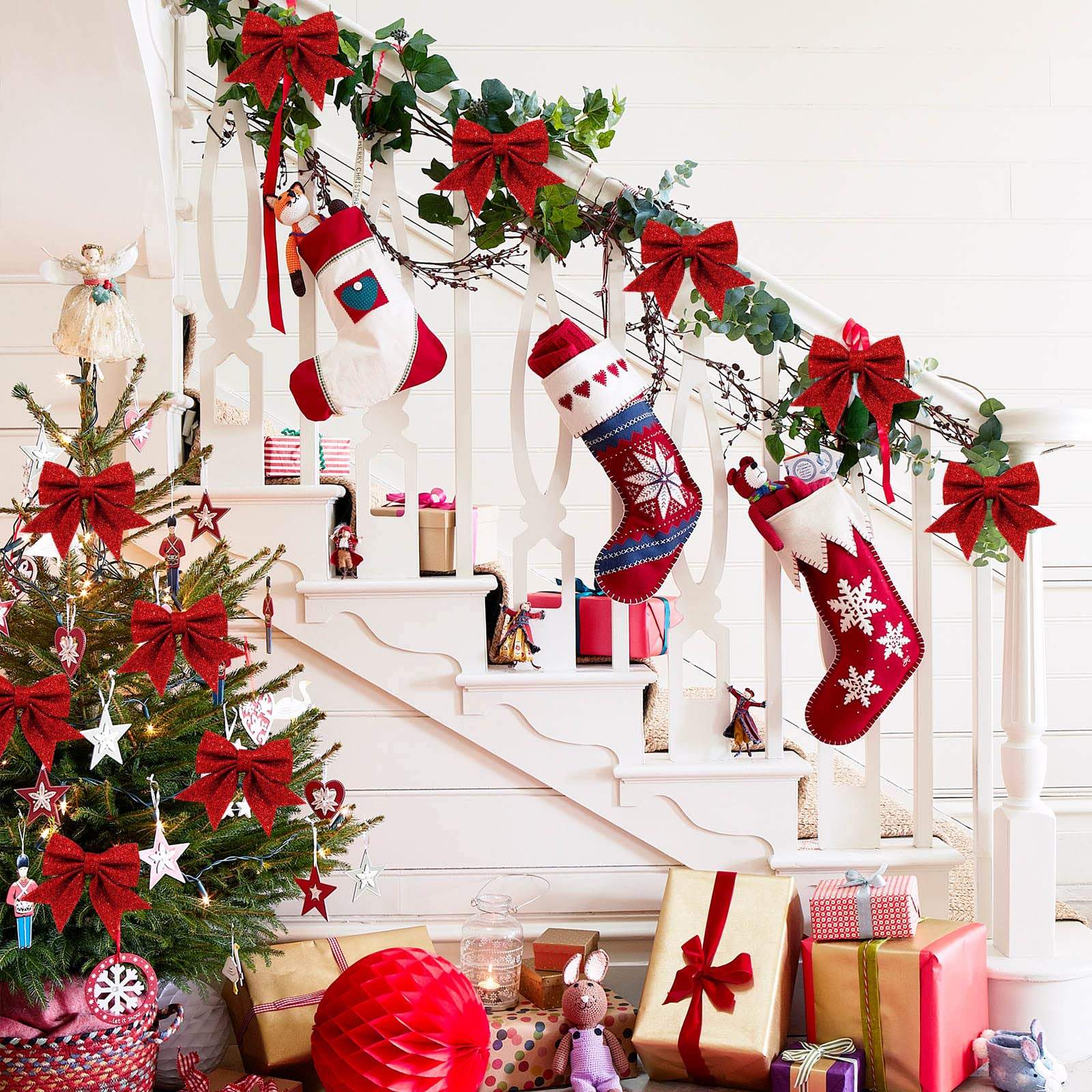 Eine Weihnachtsszene mit geschmücktem Baum, Treppe mit Strümpfen und Geschenken. Rote Schleifen und Ornamente. Warme, einladende Atmosphäre.