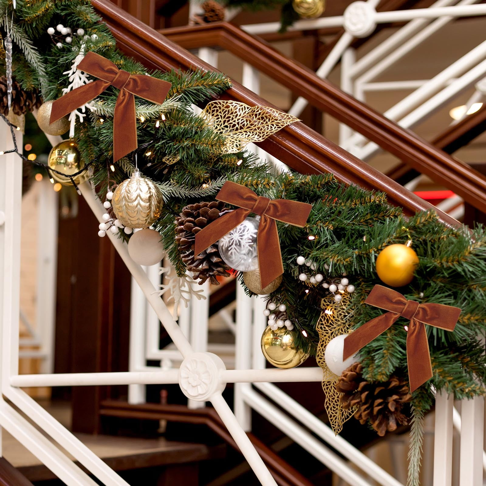 Weihnachtsdekoration auf einer Treppe. Braune Schleifen, goldene Ornamente, Tannenzapfen und Lichter schmücken den Girlande.