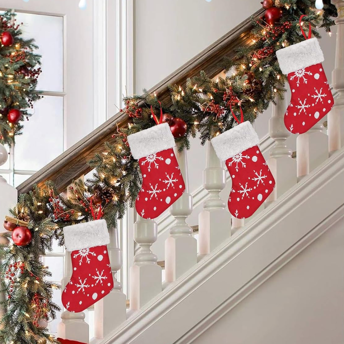 Rote Weihnachtsstrümpfe mit weißen Schneeflockenmustern hängen an einer Treppe, die mit Girlanden und Lichtern geschmückt ist.