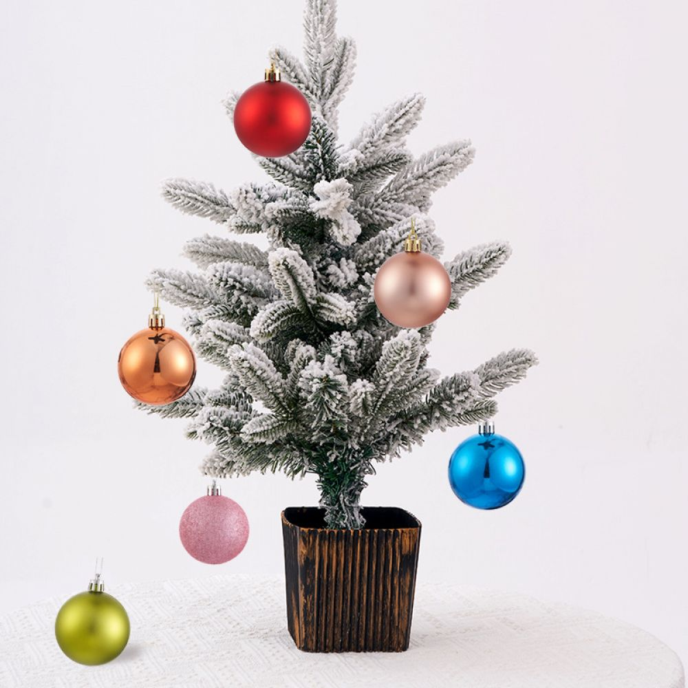 Ein kleiner Weihnachtsbaum mit bunten Ornamenten. Der Baum steht in einem dekorativen Topf auf einer weißen Oberfläche.