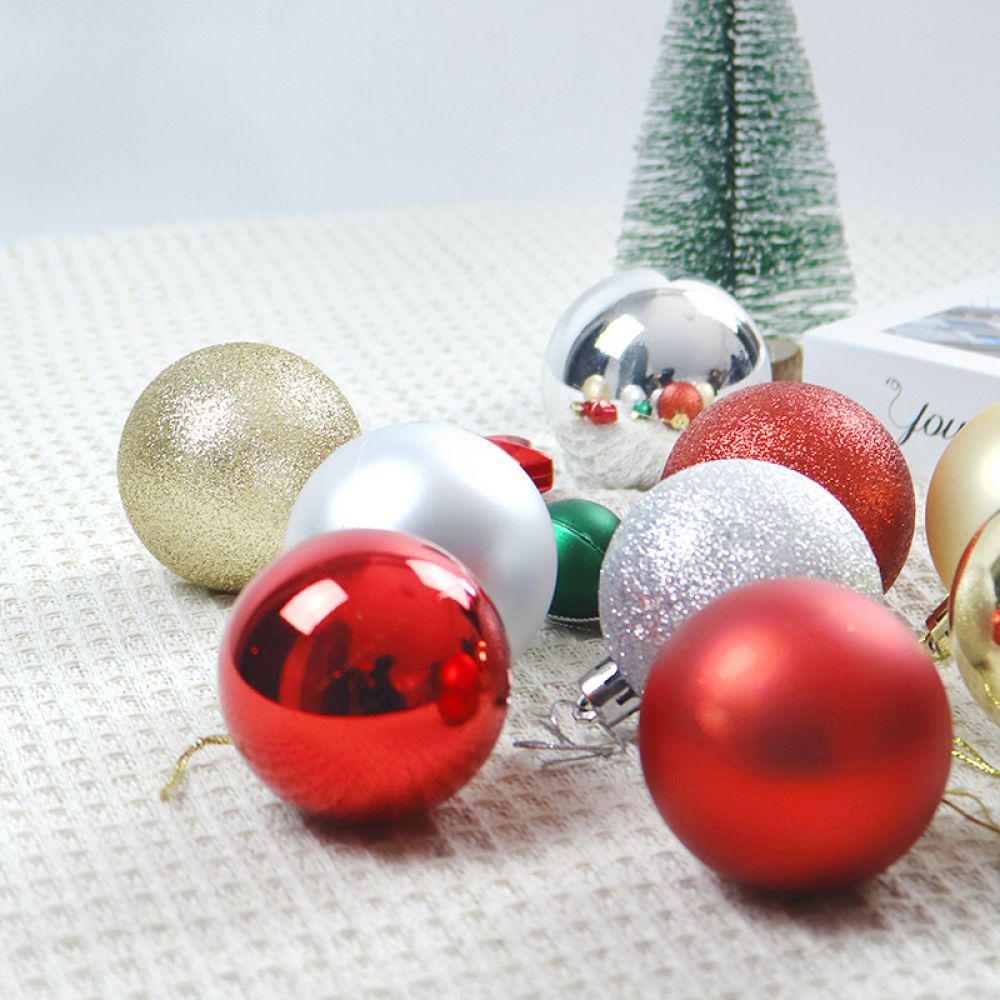 Verschiedene Weihnachtskugeln auf weißem Untergrund, darunter rote, silberne und goldene Kugeln, mit einem kleinen Weihnachtsbaum im Hintergrund.