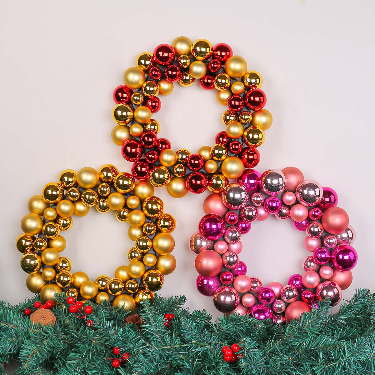Drei Weihnachtskränze aus bunten Kugeln. Gold-, Rot- und Rosatöne. Grüner Girlande am Boden. Weißer Hintergrund.