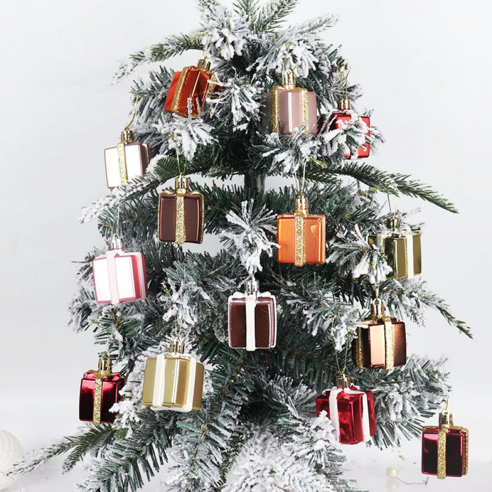 Ein Weihnachtsbaum, geschmückt mit kleinen, bunten, geschenkförmigen Ornamenten. Der Baum hat Kunstschnee, vor weißem Hintergrund.
