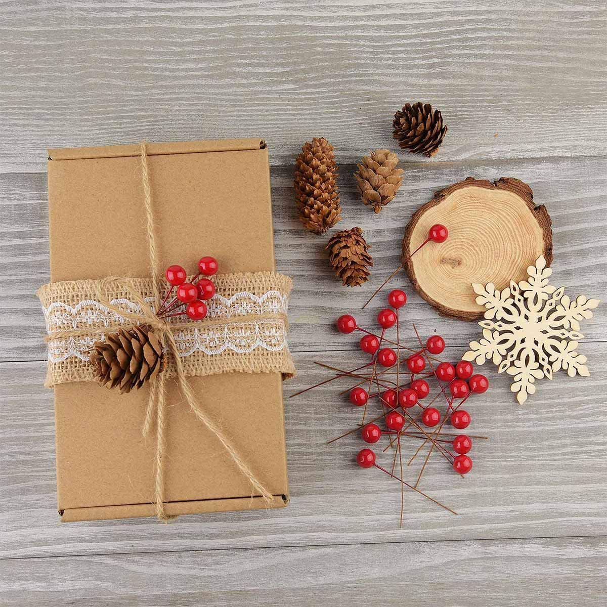 Ein Geschenkbox mit Jutegürtel, Tannenzapfen, roten Beeren, einer Holzscheibe und einem Schneeflocke auf grauer Holzoberfläche.