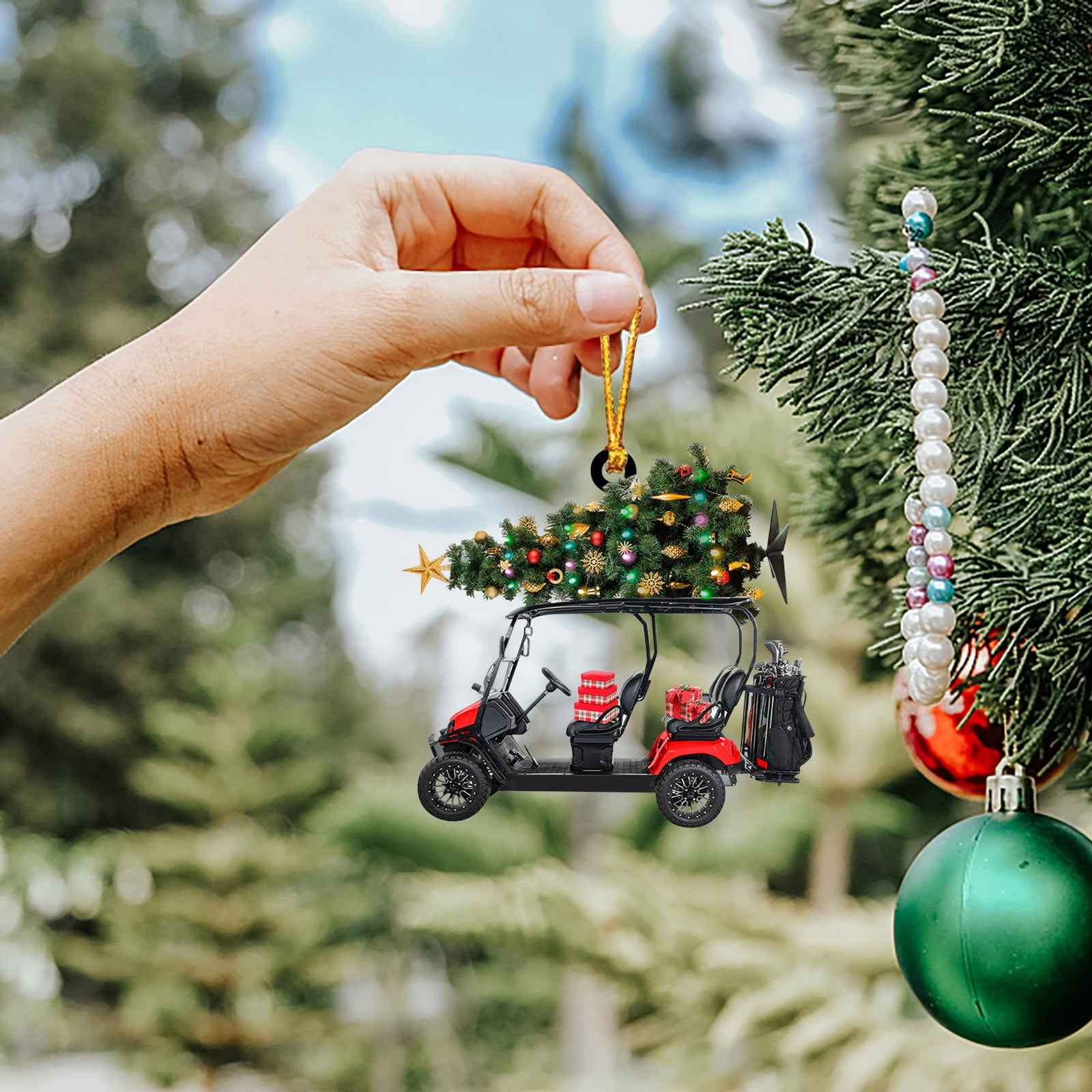 Hand hält einen Golfwagen-Weihnachtsschmuck. Der Wagen hat einen Baum, eine Golftasche und Geschenke.