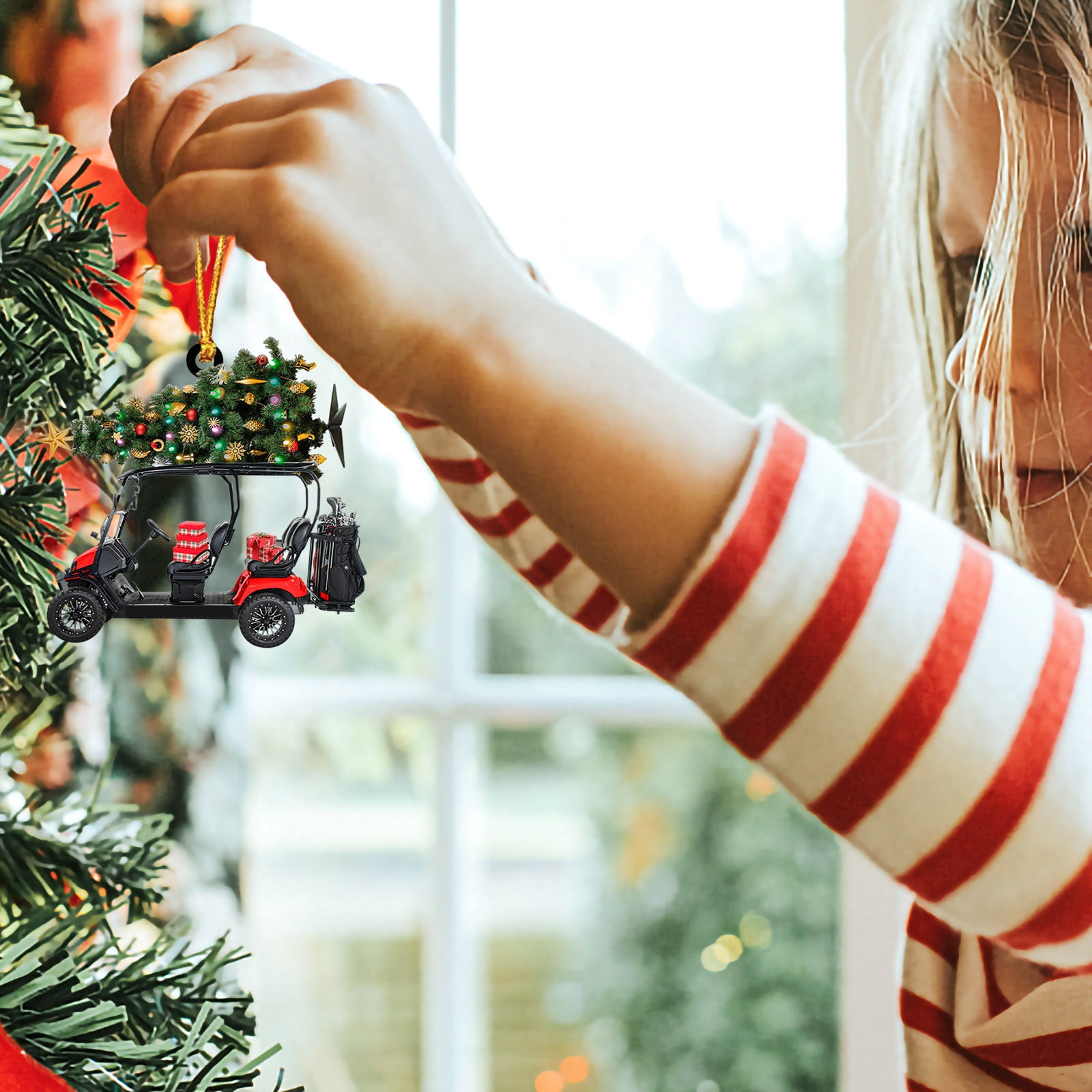 Ein Mädchen hängt einen Golfwagen-Weihnachtsschmuck auf. Der Schmuck ist rot und schwarz, mit einem kleinen Weihnachtsbaum oben.