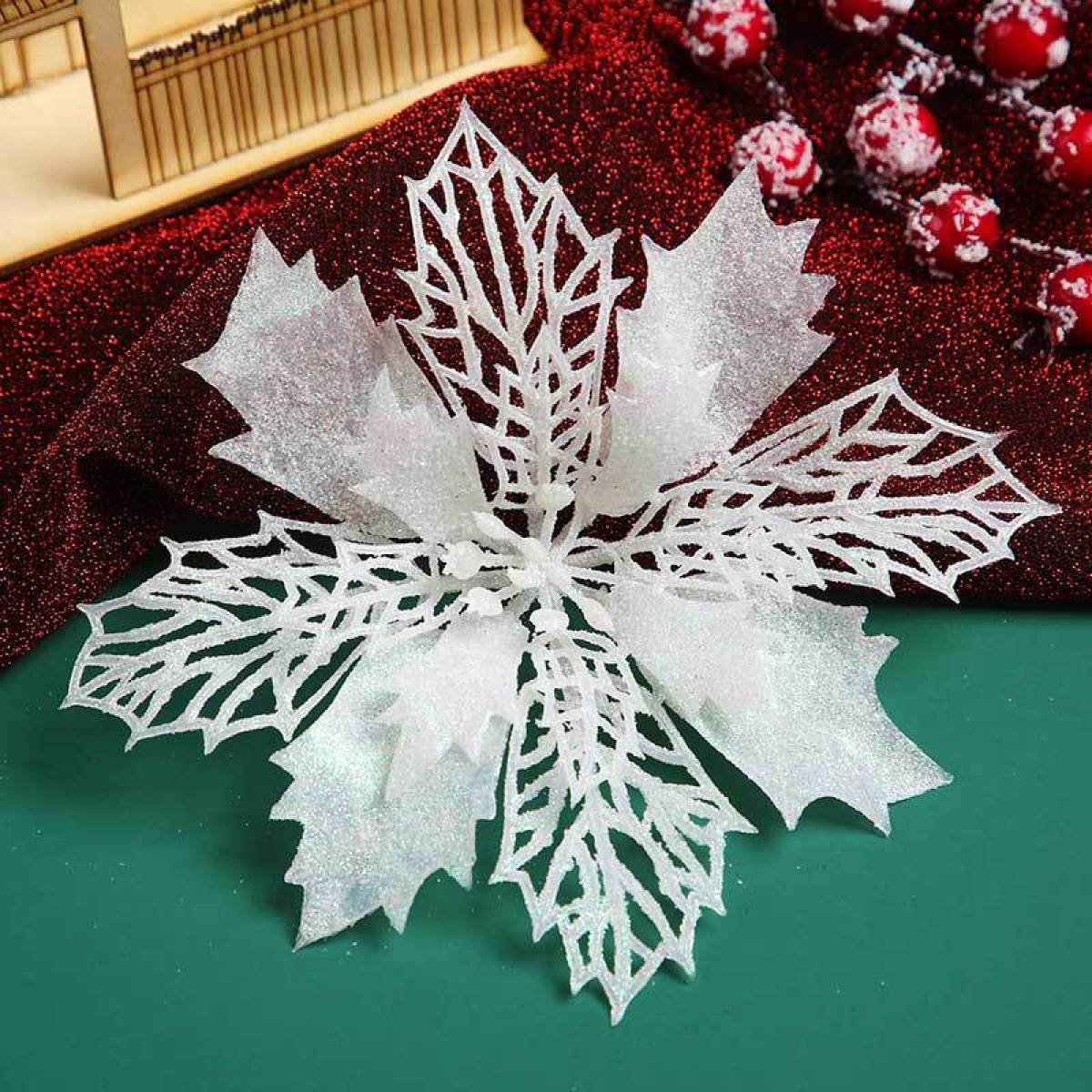 Eine weiße glitzernde Weihnachtssternblume, rote Beeren und eine Holzstruktur auf grünem Untergrund. Festliches Weihnachtsthema.