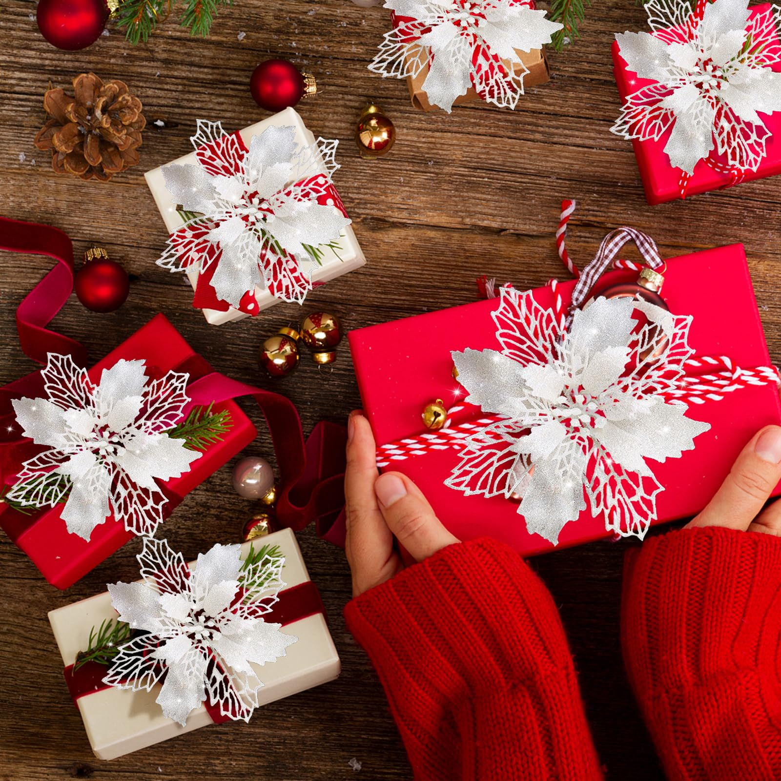 Eine Person in einem roten Pullover hält eine rote Geschenkbox. Andere Geschenke, Dekorationen und Ornamente liegen auf Holz.