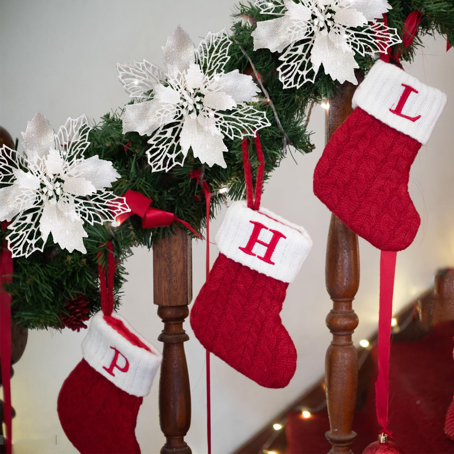 Weihnachtsdekoration mit roten Strümpfen, weißen Buchstaben und silbernen Poinsettien an einem Holzgeländer. Festlich und warm.